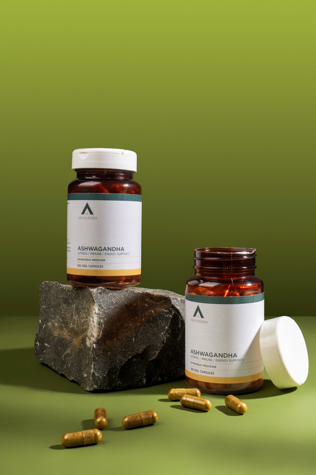 Two bottles of Ashwagandha supplements on a green background with a rock and capsules.