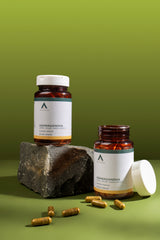 Two bottles of Ashwagandha supplements on a green background with a rock and capsules.