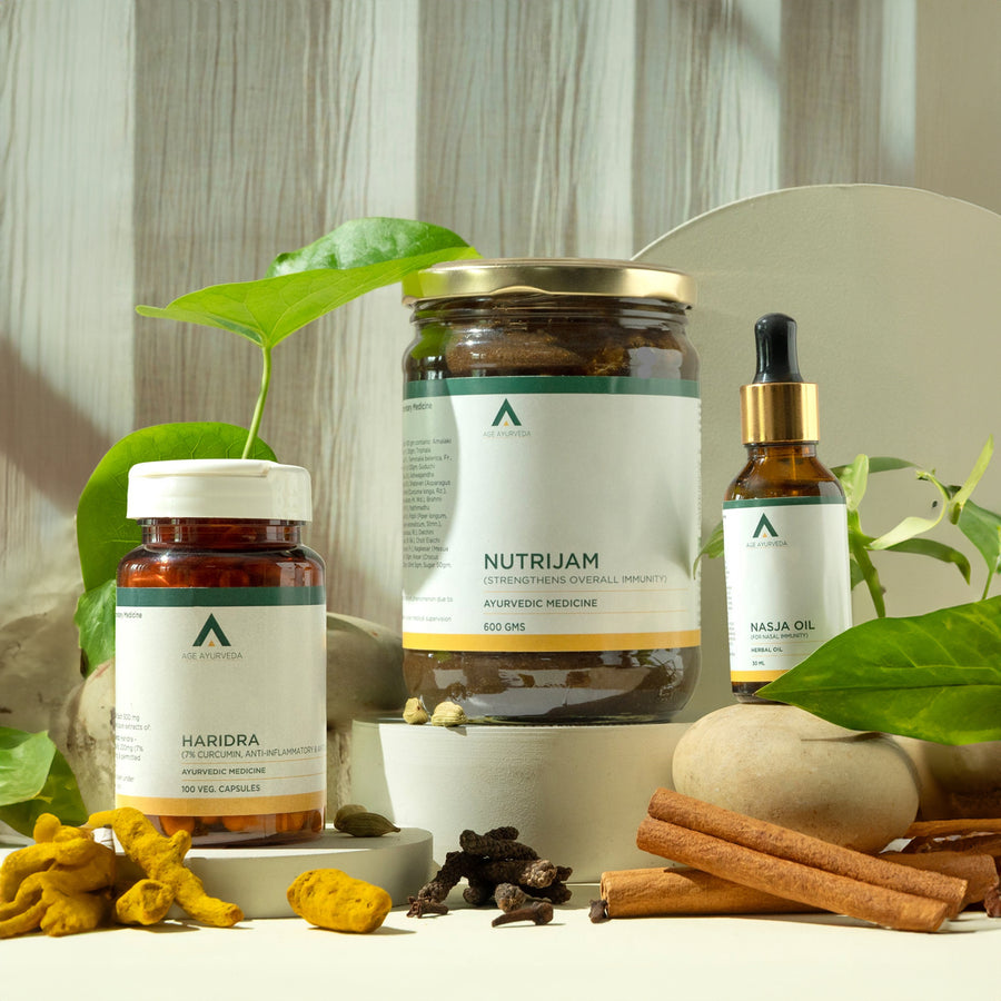 Three herbal supplement products from Aaravata Naturals are arranged on a white surface with natural leaves, turmeric, cinnamon, and whole spices. The products include a large jar of Nutrijam Ayurvedic medicine, a bottle of Haridra capsules, and a dropper bottle of Nasja Oil.